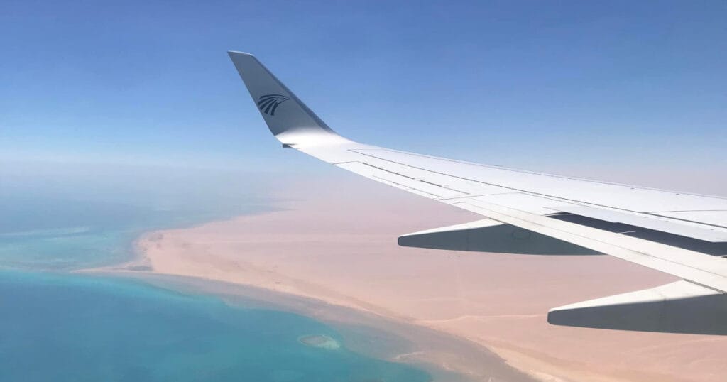 a photo of a wing of a plane flying into sharm El Sheikh over the turquoise water and sand